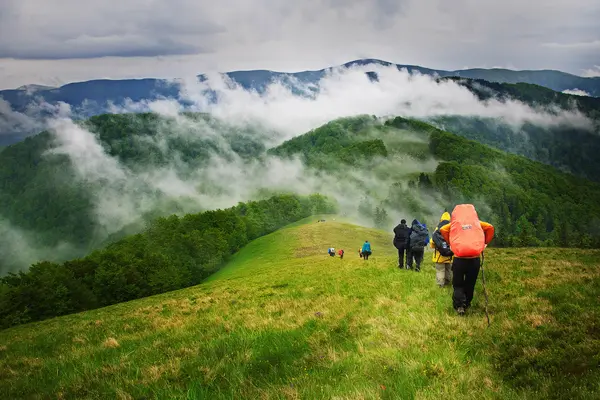 Mehrere Menschen laufen mit Wandergepäck hintereinander auf einem Bergkamm.