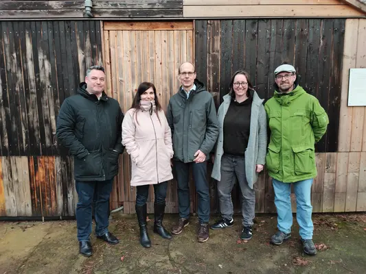 5 Personen stehen im Halbkreis vor einer Holzwand