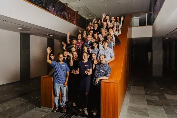 Eine Gruppe Menschen steht auf einer Treppe für ein Gruppenfoto und winkt in die Kamera.