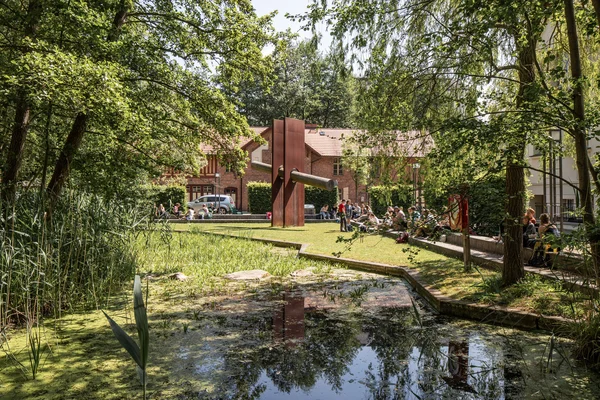 Stadtcampus der HNEE mit Studierenden und der Skulptur „Die Durchdringung“ Auf dem Stadtcampus befindet sich ein Teichbiotop, moderne Kunst und Hochschulgebäude in diversen Baustilen.