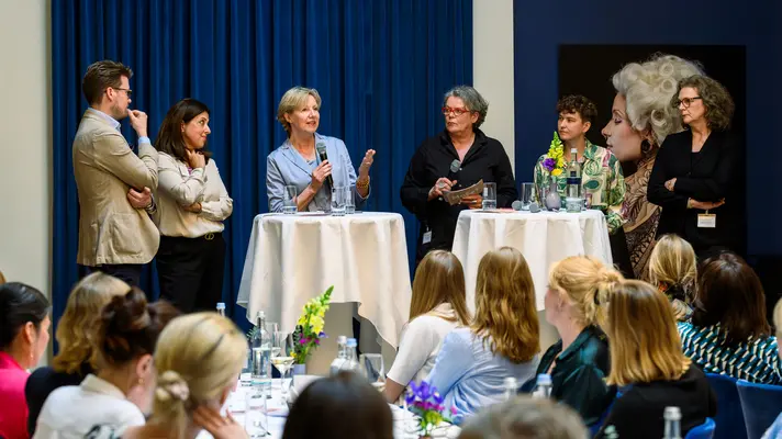 Sieben Personen stehen um zwei Stehtische und sind in eine Paneldiskussion vertieft.